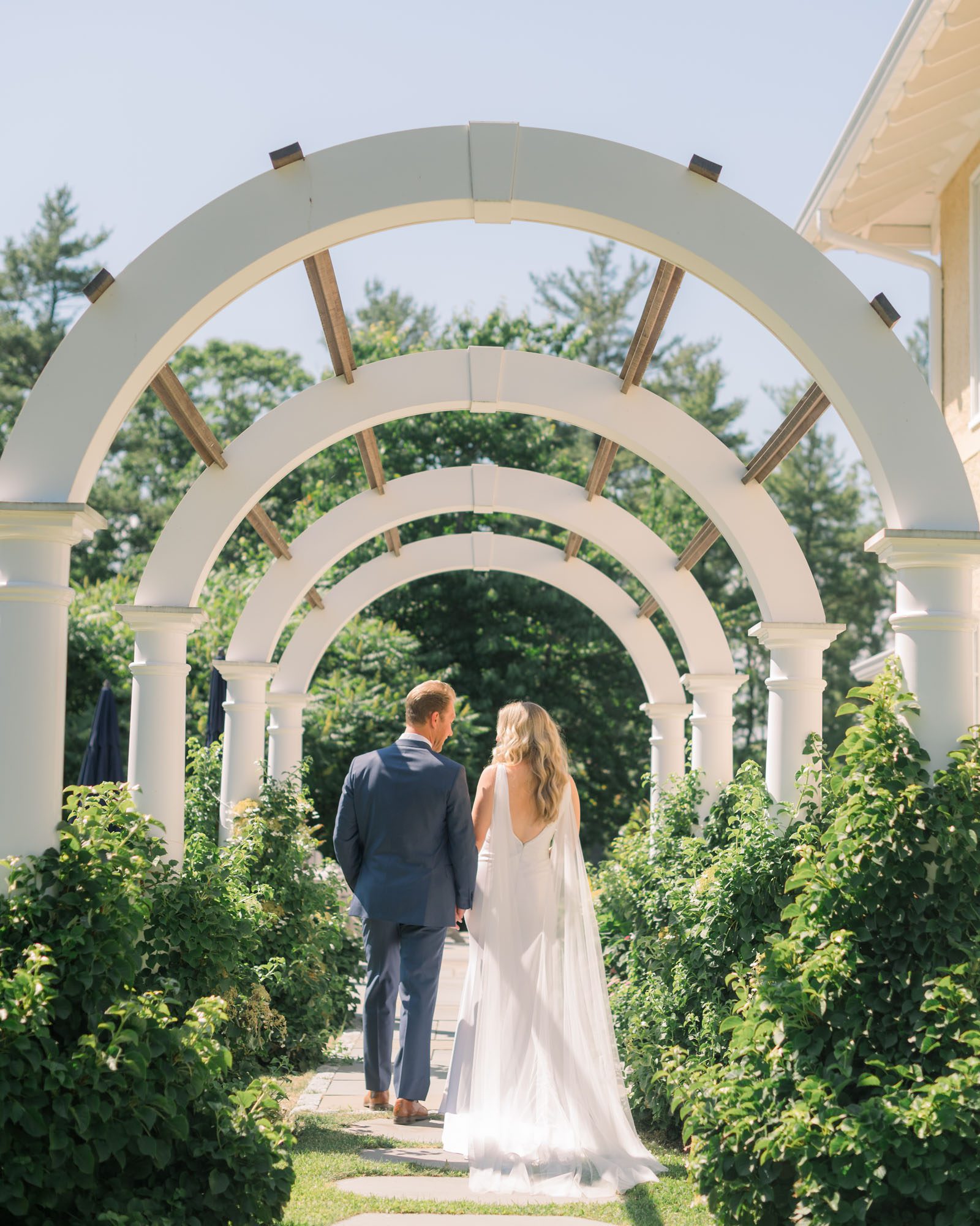 Wedding photography at York Maine private residence. Bride and groom walking under an archway.